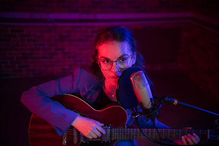 一个戴眼镜的年轻女子弹吉他唱着麦克风背景图片