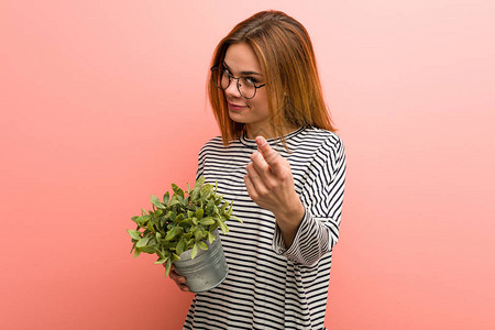 年轻女子拿着一株植物用手指着你好像背景图片