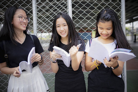 亚裔青少年持有学校书本在户外欢笑图片