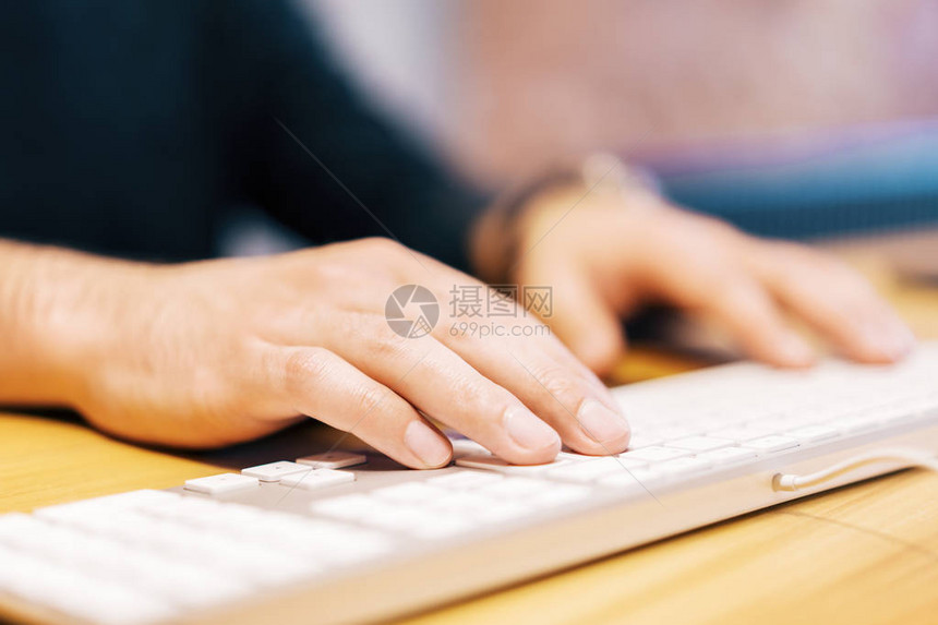 白色计算机键盘上输入男手的侧面视图Blurry背景技术图片