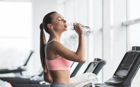 在健身房休息在跑步机上锻炼后喝水的女人图片