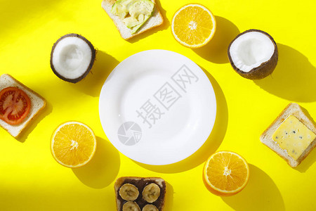 三明治配香蕉番茄鳄梨奶酪和新鲜水果橙子椰子和黄色背景上的空白盘图片