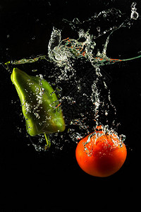 蔬菜番茄和辣椒粉在黑色背景上的水溅图片