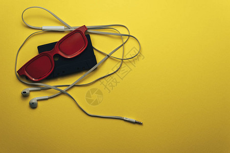 红色玻璃黑色磁带胶和白色耳机在美丽的黄色背景上图片