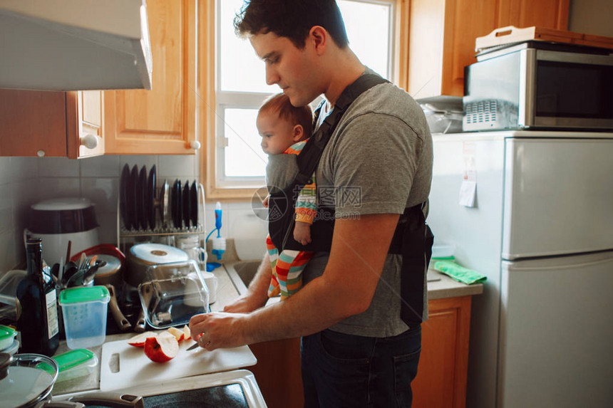年轻的白种人父亲带着刚出生的婴儿在准备午餐的载体中男人父母带着孩子站在厨房里做食物真实的生活方式坦诚真实的时刻单身爸图片