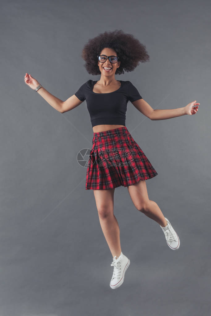 时尚的非裔美国女正在跳跃和微笑在灰色图片