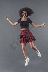 时尚的非裔美国女正在跳跃和微笑在灰色图片