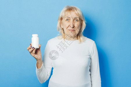 一名老年妇女在蓝色背景面前持有一瓶药丸或小药瓶图片