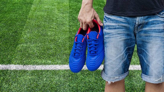 男子在足球场上手拿蓝色足球鞋图片