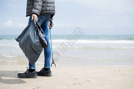 一个白人男子在孤独的海滩上用垃圾收集棒收集垃圾的特写镜头图片