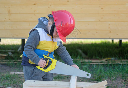 男孩戴硬帽手锯木板年轻木匠在新图片