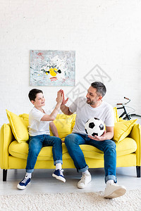 父亲和儿子在家用足球坐在沙发上时图片