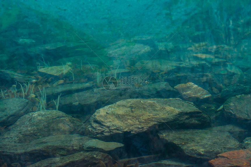 山湖底部的巨石和植物与干净的水特写山反映在光滑的水面上背图片