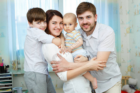 年轻家庭的肖像与两个男孩的男孩拥抱微笑和在儿童房间里看相机片一样图片
