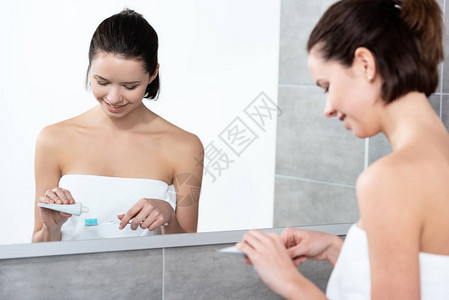 年轻妇女在浴室镜子附近的牙刷上图片