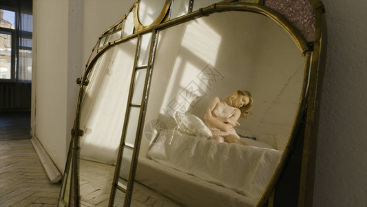 一个穿着睡衣的漂亮金发女孩躺在白床上弯下双腿动图片