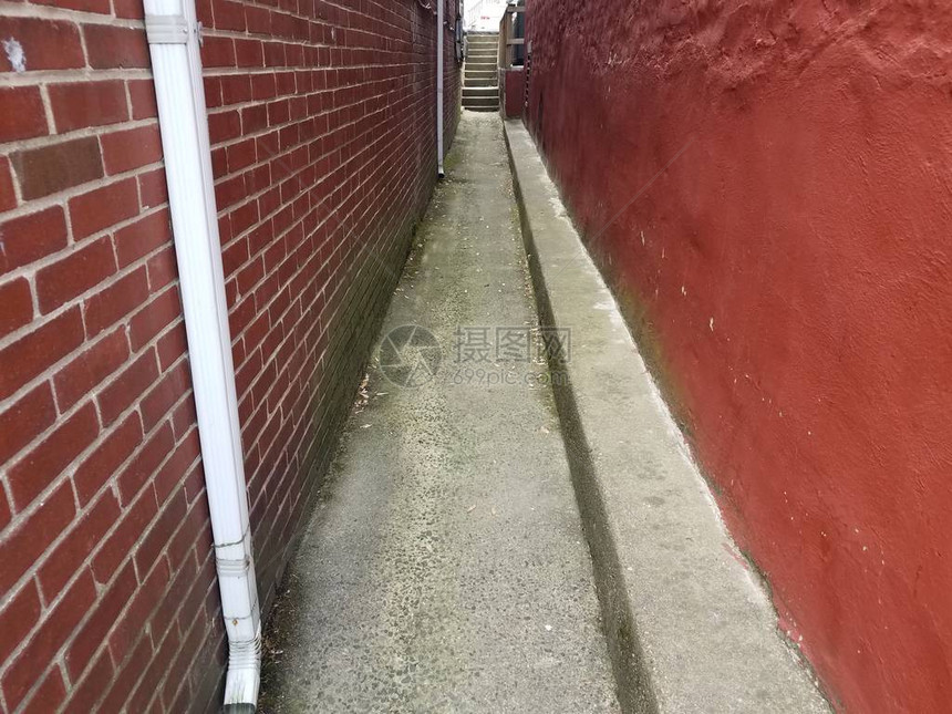狭窄的巷子有红墙和砖块在泥图片
