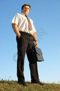 身穿白衬衫带着黑色公文包站在草地上与黑色公文包对准蓝天图片