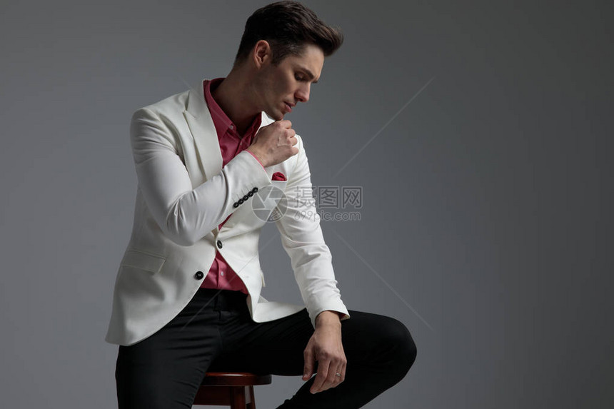 一个穿着西装的坐着的帅哥在灰色背景下把胳膊放在腿上图片