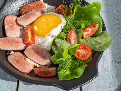 用香肠樱桃西红柿和叶子生菜在黑圆锅上的炒鸡蛋的丰盛早餐图片