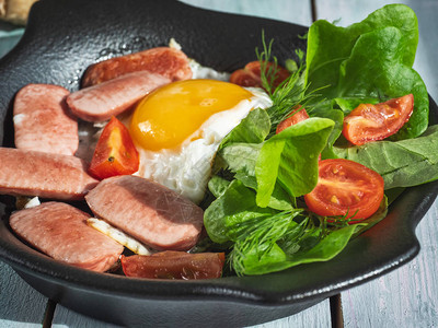 用香肠樱桃西红柿和叶子生菜在黑圆锅上的炒鸡蛋的丰盛早餐图片