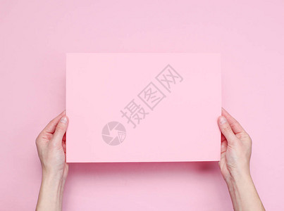 女手握着粉红背景的粉红色纸页背景图片