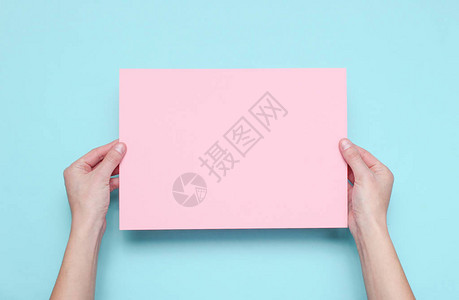 女手握蓝色背景的粉红色纸页背景图片