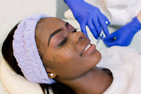 整形外科年轻的非洲妇女在嘴唇上注射化妆品美丽的非洲女人为嘴唇注射美图片
