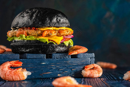 芝士汉堡配虾在木制蓝色背景上的黑色小圆面包图片