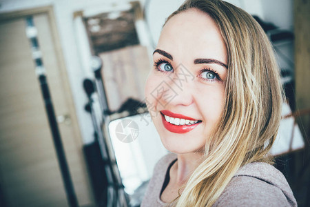 微笑着年轻的欧洲金发女郎在她工作室的公寓里做图片
