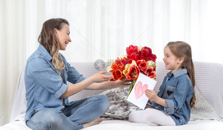 母亲节快乐带着一大束郁金香的可爱小女儿祝贺她的母亲在客厅的内部图片