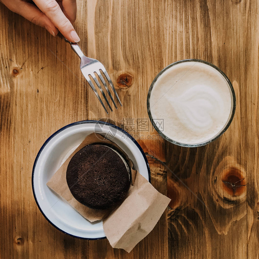 木制桌上的咖啡和巧克力蛋糕手牵着叉子碰蛋糕拍图片