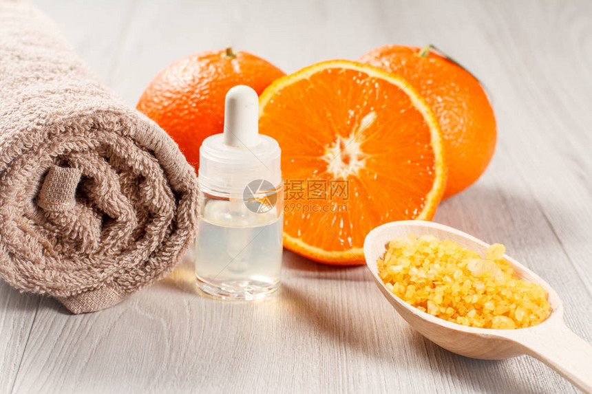 用两个完整的橙子毛巾香薰油瓶和木桌上的黄海盐木勺切橙子水疗产品和配件选图片