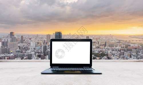 电脑笔记本电脑空白屏在白色混凝土桌上和日本大阪市日落景观笔图片