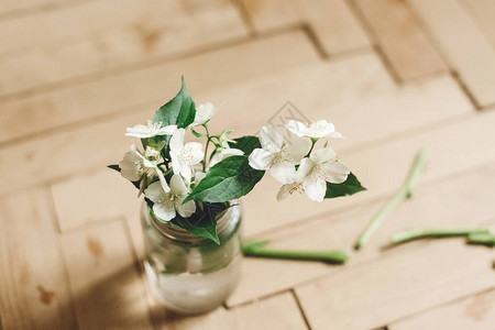 美丽的茉莉花在质朴的旧木地板上的玻璃罐中的树枝上图片