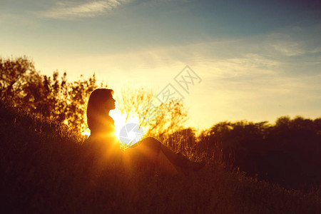 夕阳下坐在山上的年轻女子的剪影图片