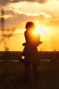 一个美丽梦幻般的女孩在日落时分在田野里穿着裙子的剪影图片