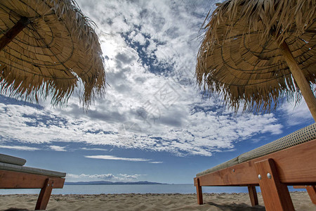 有稻草沙滩伞木制日光浴床沙滩海岸和蓝色大海图片