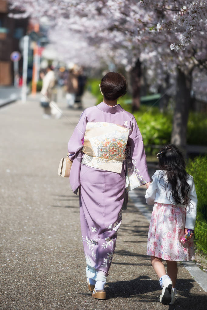 身着传统和服连衣裙的日本母亲与女儿一起在日本名古屋的山崎河边欣赏樱花或樱花春季著名的旅图片