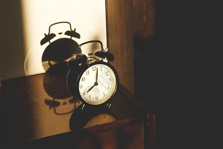 木制床边桌子上的黑色古老闹钟背景图片