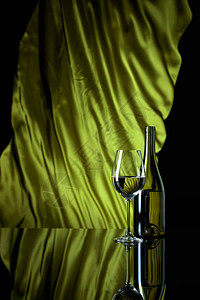 黑色反射背景的酒杯和白葡萄酒瓶子绿色沙丁鱼窗帘在风中闪图片