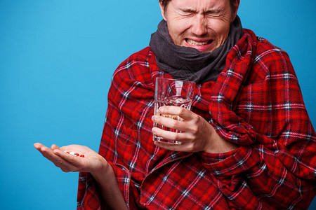 裹着毯子的病人手上拿着平板和杯子站在蓝色背景上图片