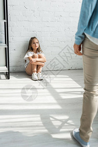 坐在地板上看着母亲的不开心的孩子有图片
