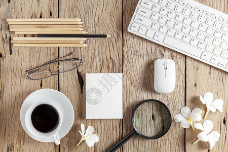 键盘鼠标白咖啡杯白皮书铅笔眼镜放大镜和鸡蛋花在旧木桌背景图片