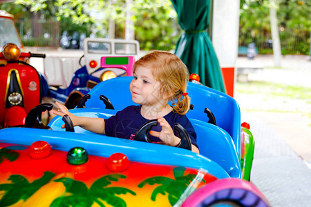 可爱的蹒跚学步的小女孩在游乐园的回旋处转木马上骑着有趣的车快乐健康的宝贝孩子在阳光明媚的日子在户外玩得开心家背景图片