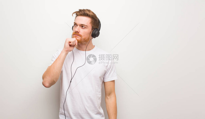 年轻红发男子怀疑和困惑用耳机听图片