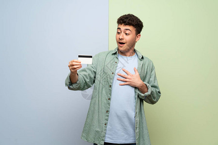 蓝色和绿色背景的年轻人拿着信用卡很惊讶图片
