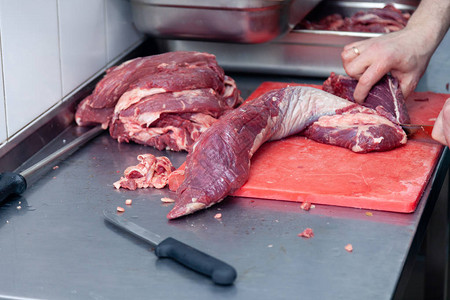 男子屠夫厨师在红色塑料板上用刀切下里脊肉片生牛肉和猪肉的特写手农贸市场烧烤用背景图片