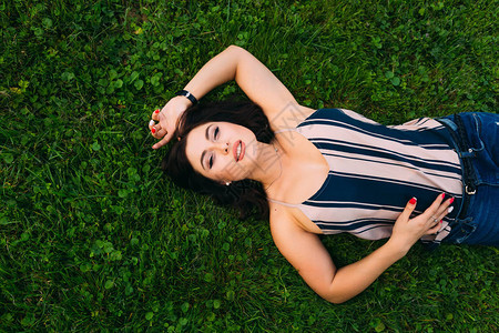 一位年轻女子躺在绿色草地上看着摄像图片