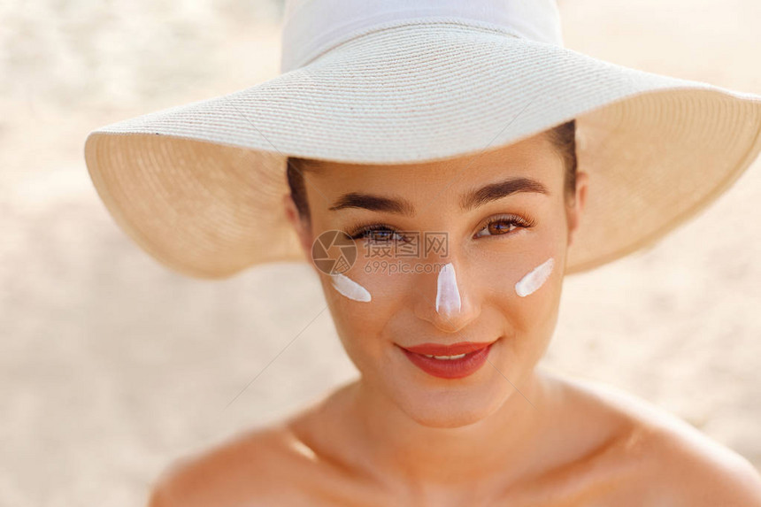 女人微笑着在脸上涂抹防晒霜皮肤护理身体防晒防晒霜戴帽子的女在皮肤上图片